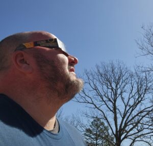 Guy wearing solar eclipse viewing glasses looks towards the sun